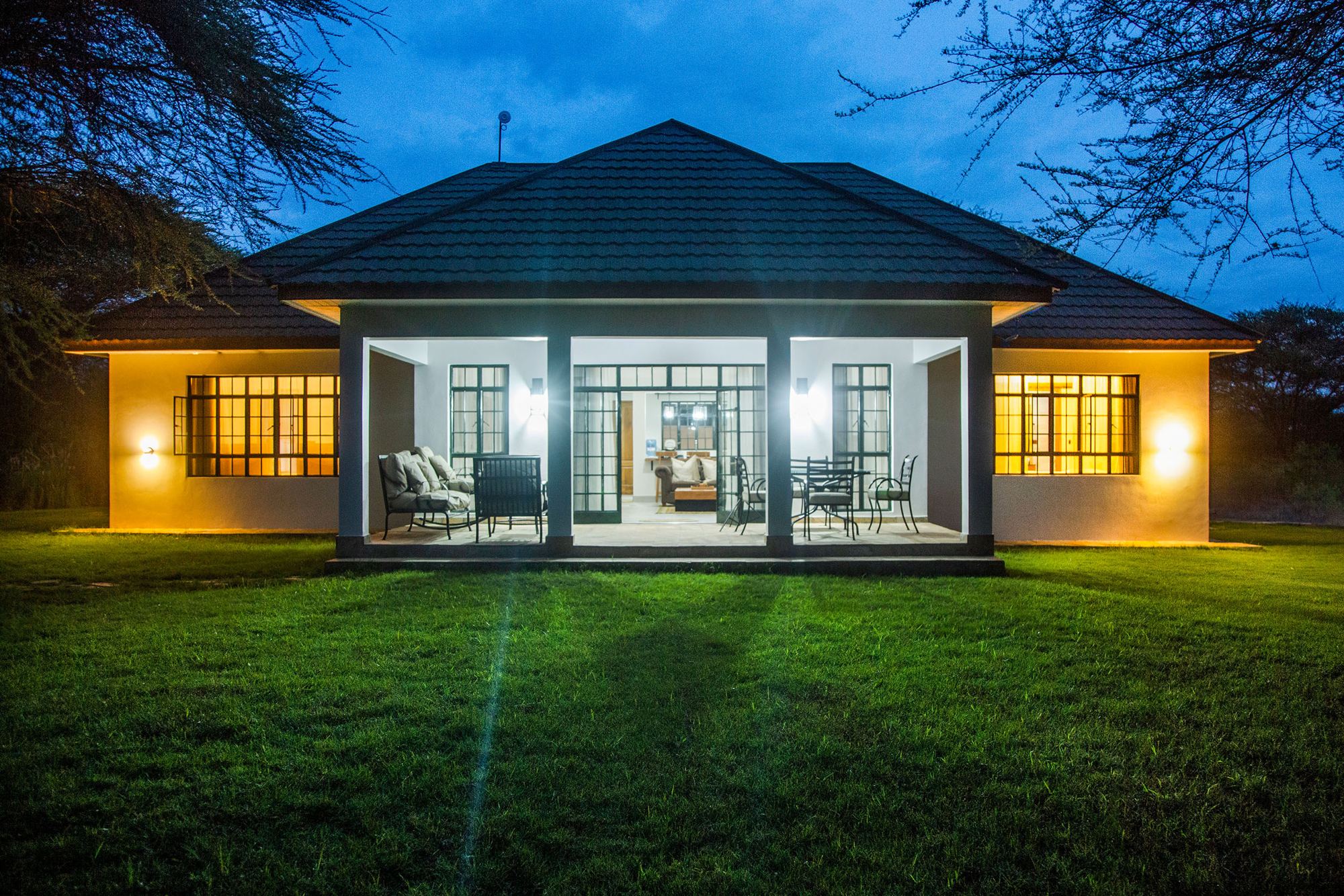 Kili Meru Cottage lit up at dusk across the lawn, Usa River